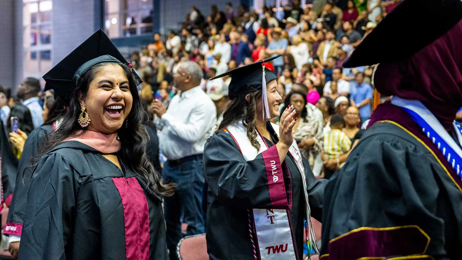  A graduate with an East Indian bindi grins excitedly as she walks the stage at Commencement