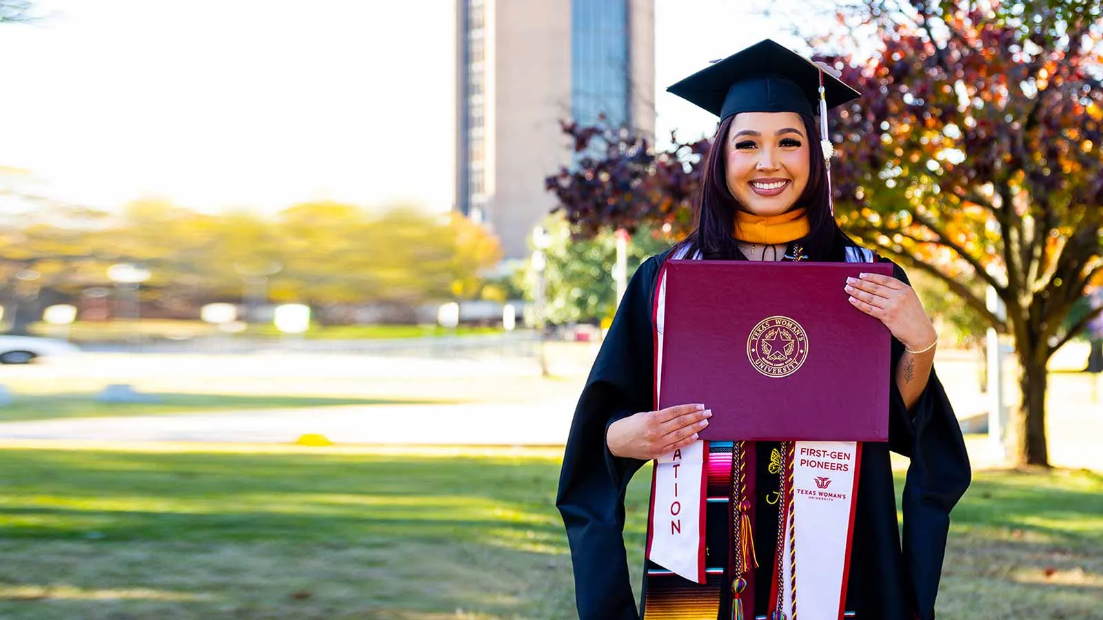 A ̽��¥ student in graduation regalia holding up a diploma