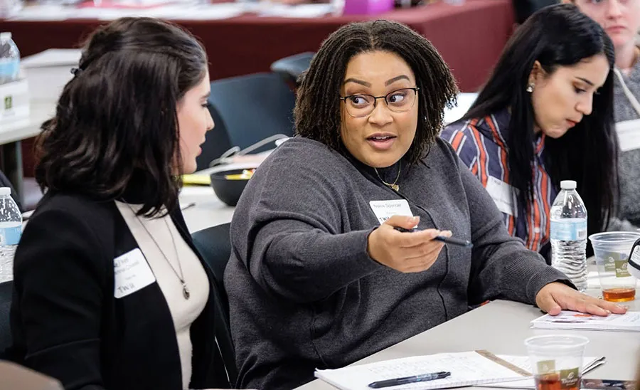 Students talking at a classroom table. 