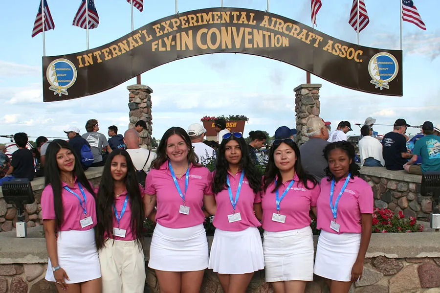 Six students standing under the entrance sign of the EAA AirVentures show. 