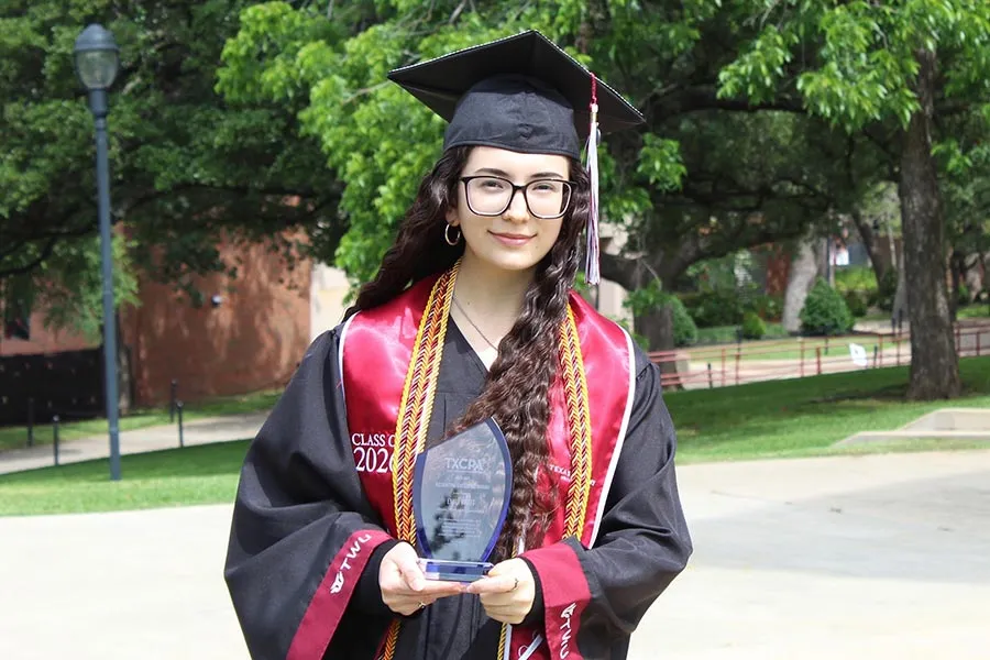 Emily Kraft holds a glass award, dressed in graduation robes