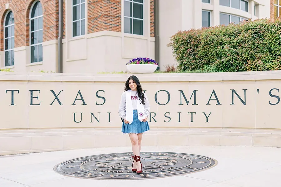 A Texas Woman's graduate stands in front of the Texas Woman's University sign