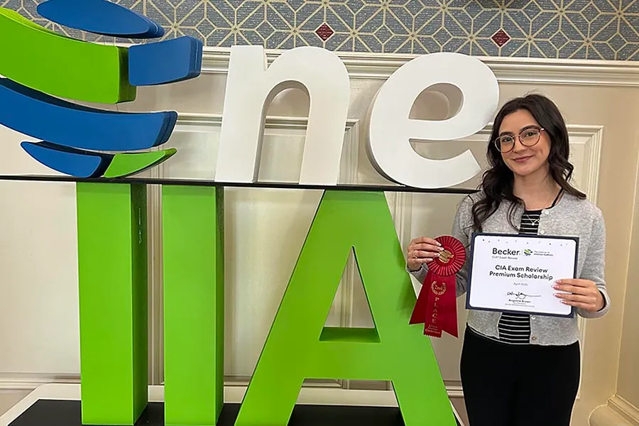 Leslie Frias in a white top holds up a certificate next to a large The Institute of Internal Auditors (IIA) logo