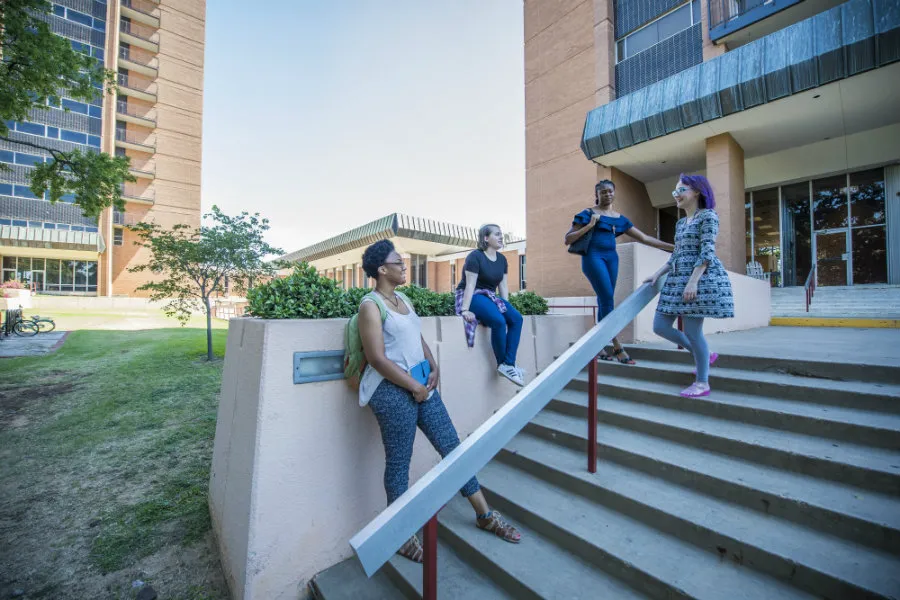 Four young women talking and relaxing on the stairs outside the Stark Hall dorms.