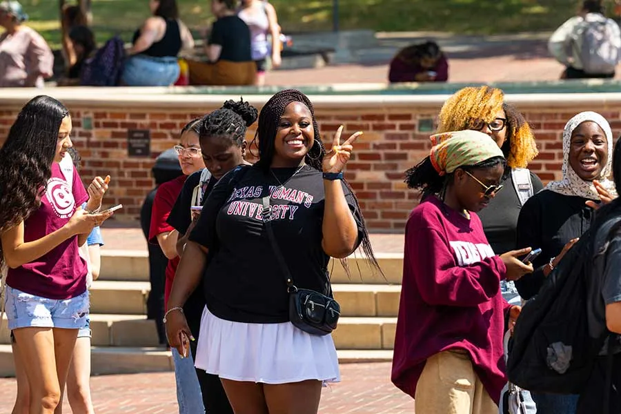 A TWU student at a busy events holds up a peace sign and smiles at the camera. 