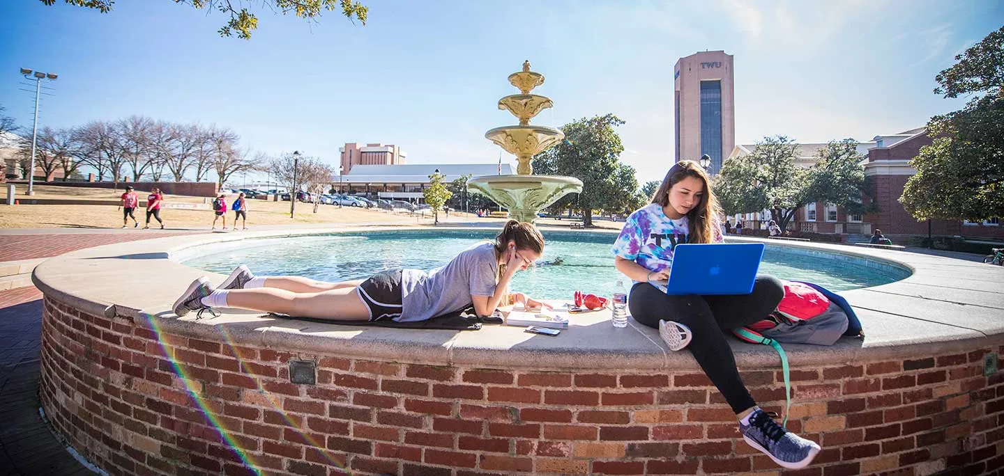 Two students study outdoors on TWU's Denton campus fountain.