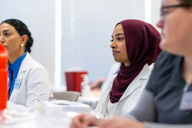 A TWU Nurse Practitioner students sits in a nursing sim lab classroom setting.