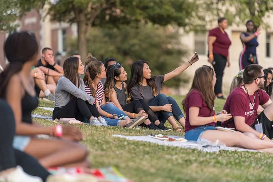 A group of TWU students relax on the lawn in front of Hubbard Hall and take a selfie.
