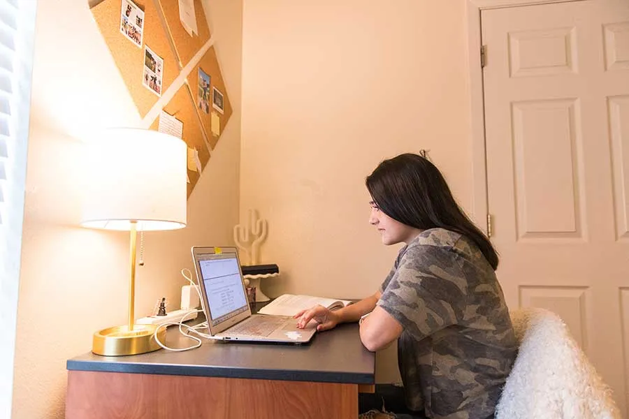 A student works from home on a laptop at a desk.