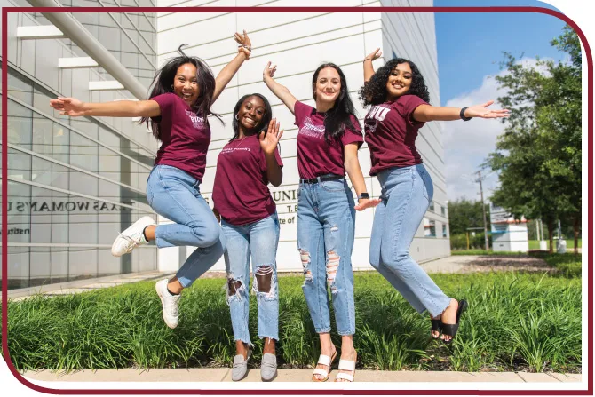 Four students smile and jump in the air on a university campus.