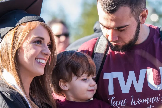 A TWU graduate smiles with her spouse and child after commencement.