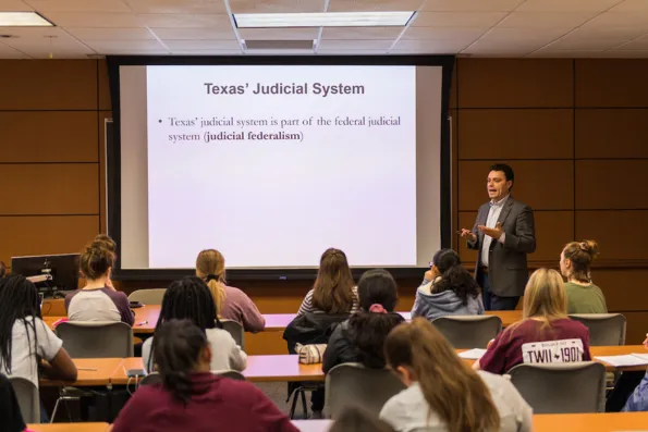 A photo of a professor giving a lecture to a room of students. A projector screen shows notes for legal studies terms.