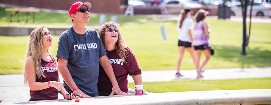 A TWU student and her parents relax at the fountain on a sunny day. 