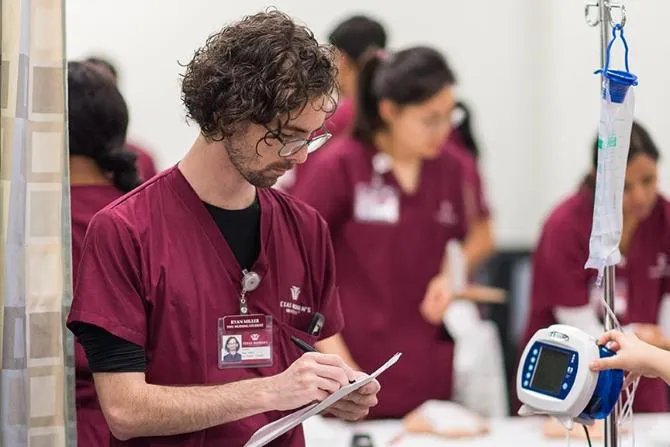 A male nursing student writes down patient vitals on a clipboard