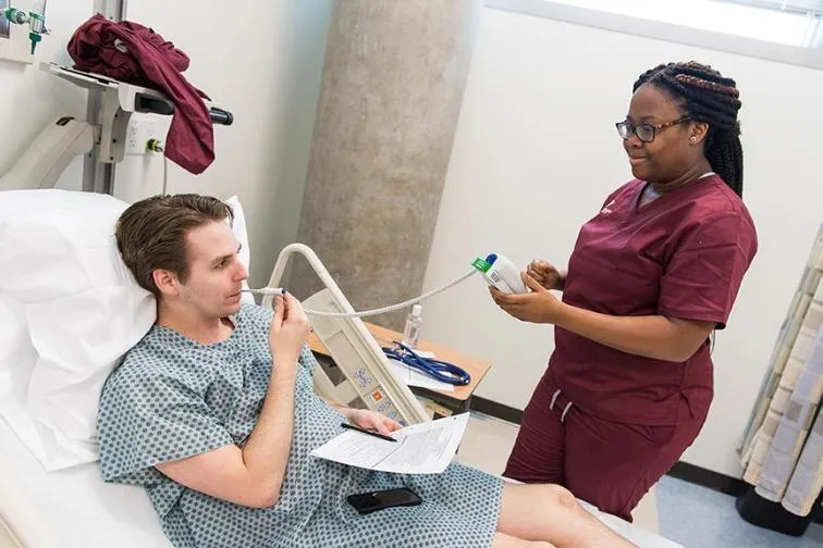 A TWU nursing student takes the temperature of a patient in a hospital bed