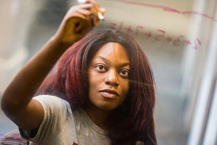 A TWU student works a math equation on a clear board