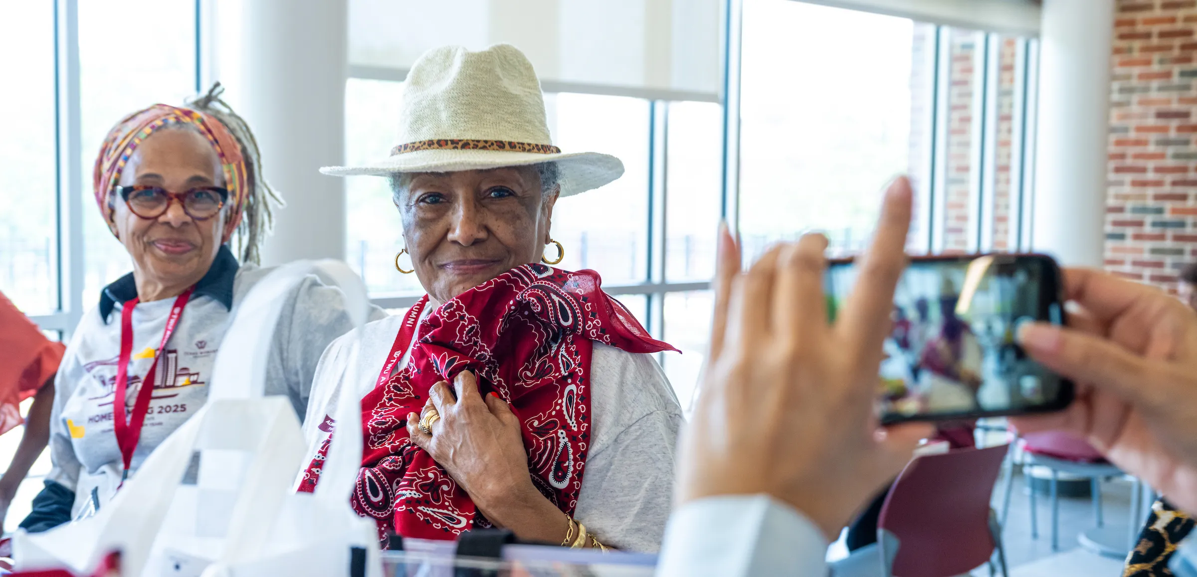 Two alumni wearing maroon bandanas pose smiling for a photo at the 2025 Homecoming 