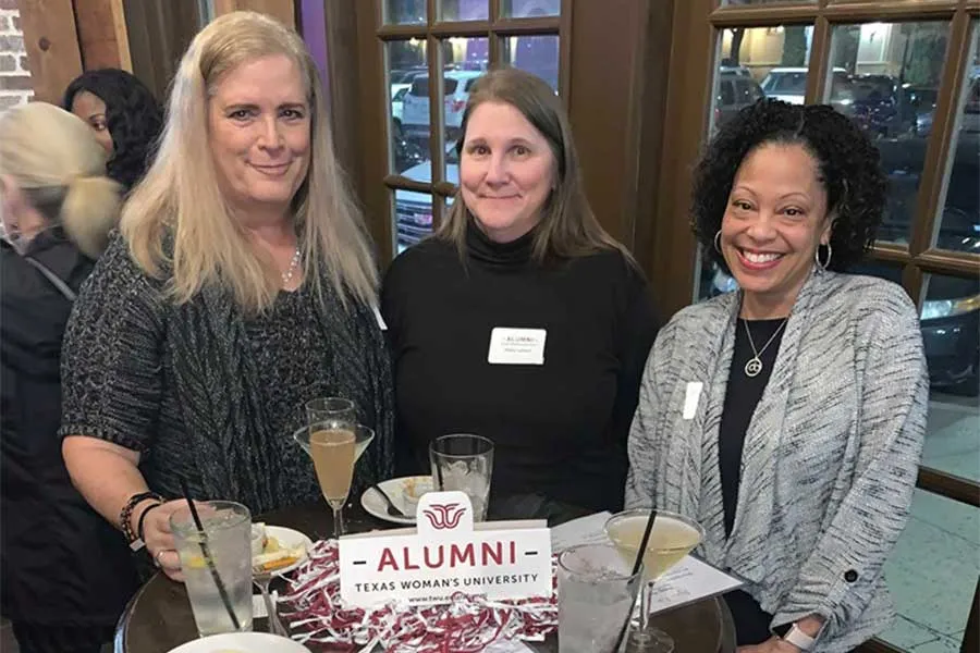 Three TWU alumni enjoy drinks at a table during an alumni event.