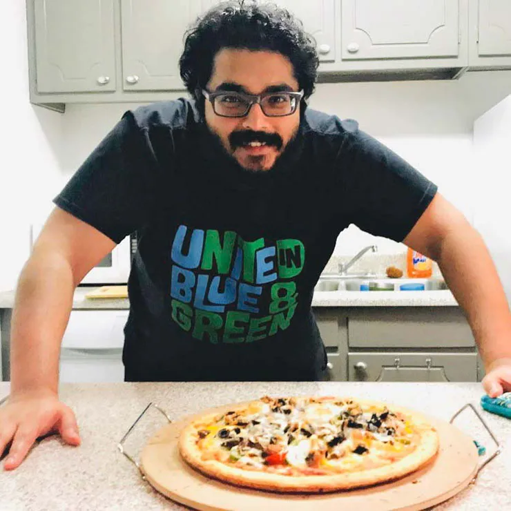 TWU alumnus Dr. Rishi Raj stands in an industrial kitchen in front of a homemade pizza