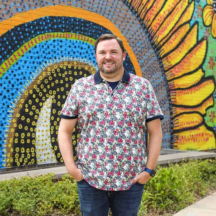 Brett Dyer standing in front of his mural 'The Proof is in the Flowers'