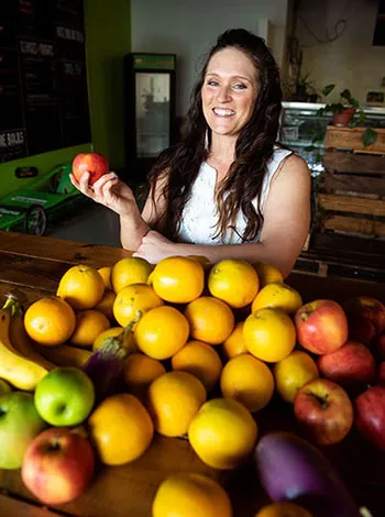 Loni Puckett stands in front of a large bowl of fresh fruit, holding an apple in her hand.