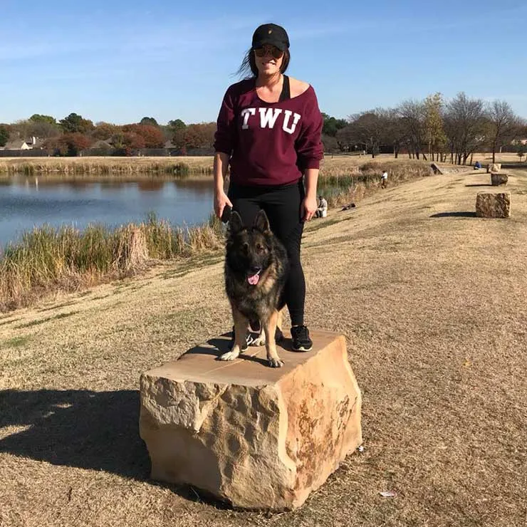 Loni Puckett stands outside on top of a large stone with a German Shepherd dog.