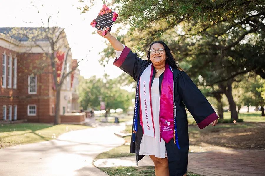 Magali Castillo Nicolas stands in graduation attire, holding her cap in an outstretched hand