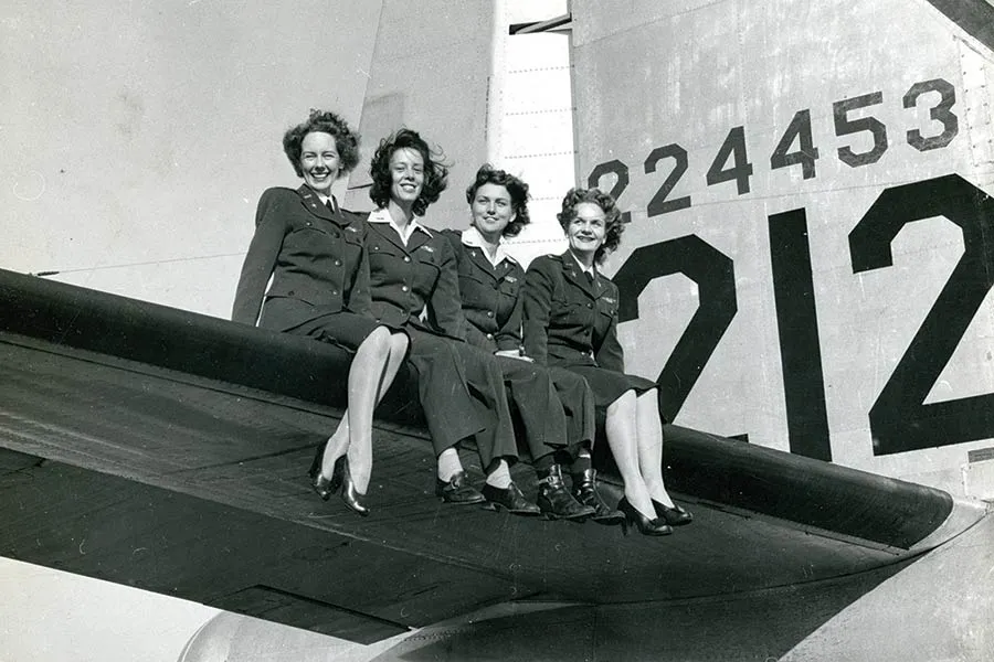 Four Women Air Force Service Pilots (WASPs) sit on the wing of a fighter aircraft