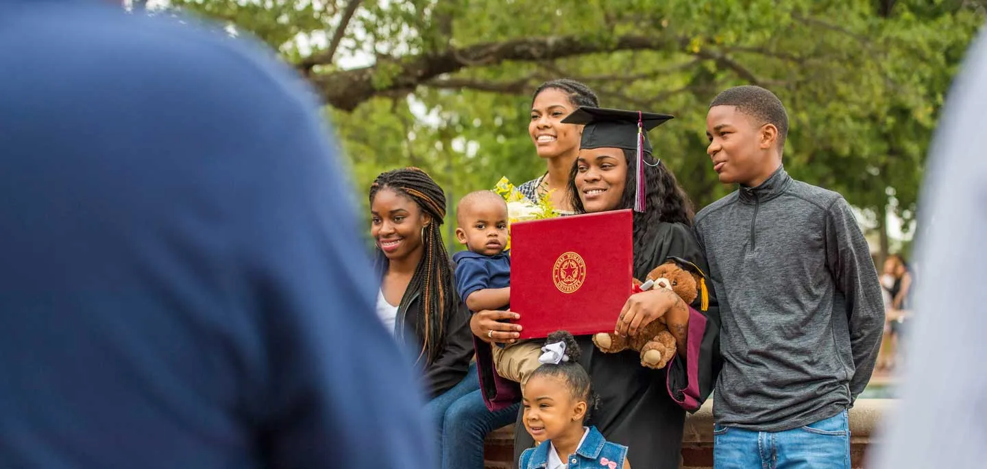 A woman with her family smile outdoors on the TWU Denton campus at commencement.