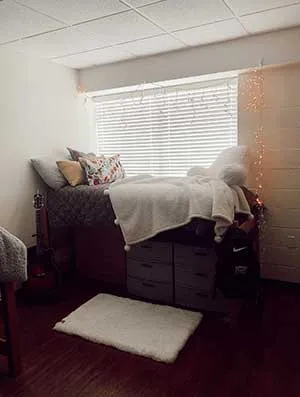 A TWU Guinn Hall dorm room with a nicely decorated bed and rug in view.