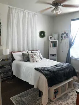 A white and navy decorated dorm room with a curtain and lights over the bed.