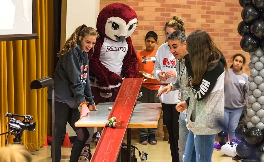 TWU mascot Oakley watches as a group of kids test their Edible Car submission by rolling it down a ramp