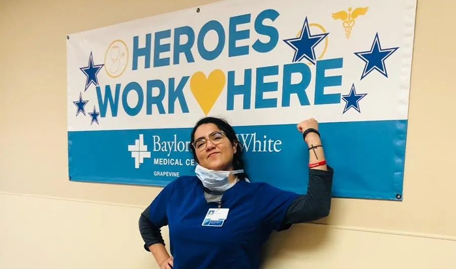 TWU social work graduating senior stands in front of a sign for Baylor, Scott and White Medical Center that reads 'Heroes Work Here'.