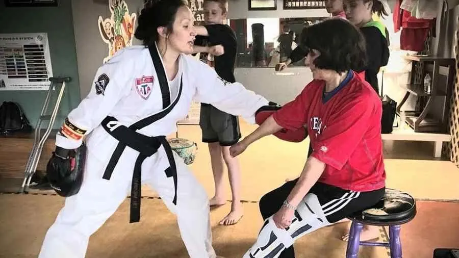 Christina Hill works with a woman in a full leg brace on martial blocks