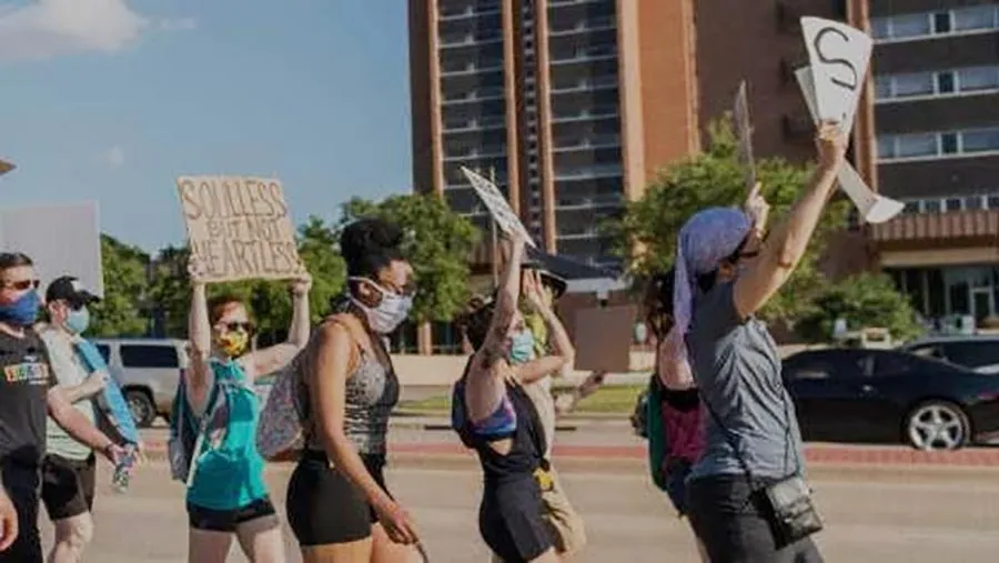 Protestors march outside the TWU Denton campus, wearing protective masks and holding signs