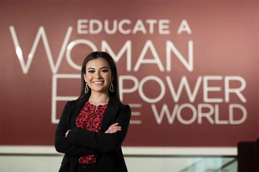 A woman in business attire stands in front of a backdrop that says 'Educate a Woman, Empower the World'