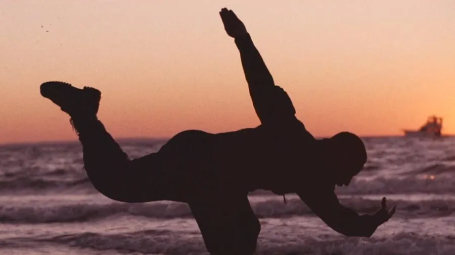 The silhouette of a man dancing in front of an ocean at sunset