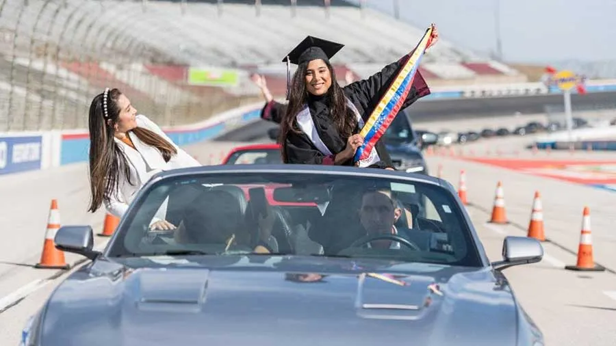 A TWU graduate stands up in a convertible holding a banner as the car crosses the finish line at the Texas Motor Speedway