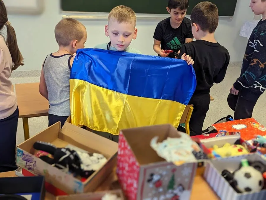 A small Ukrainian child holds up the blue and yellow Ukrainian flag in a classroom