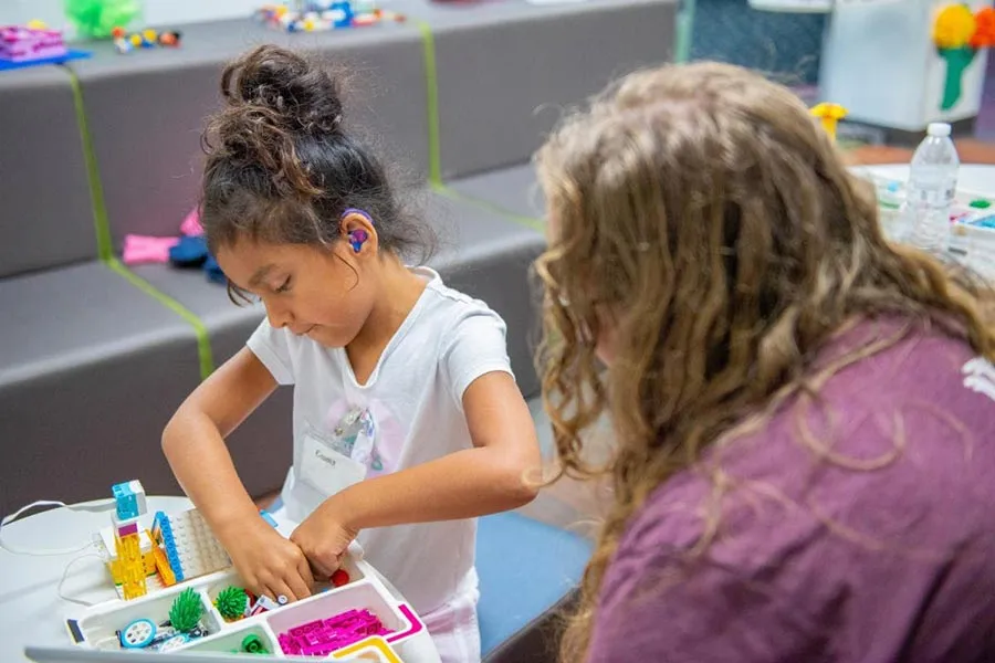 A young hearing-impaired child builds a science project with Legos under the guidance of an instructor