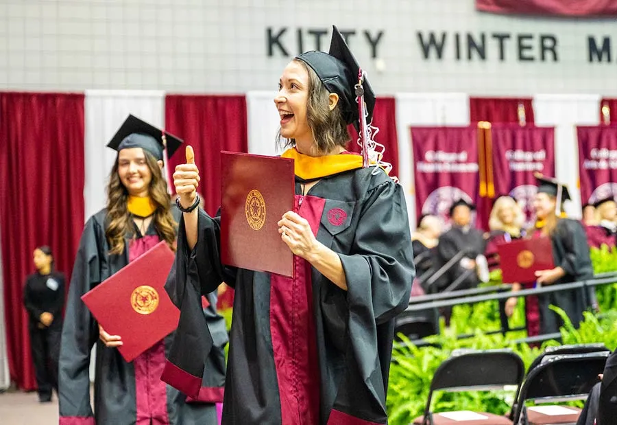 A TWU graduate proudly holds up her diploma during Commencement