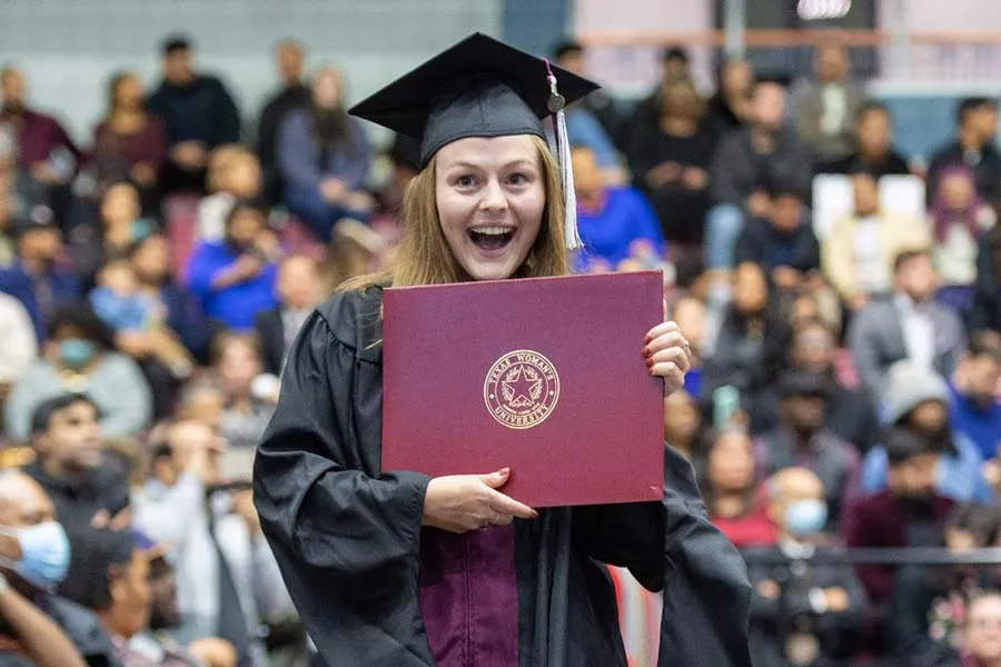 A TWU graduate holds her diploma with an excited grin