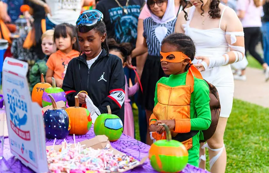 Two small children in Halloween costumes choose candy from a table at TWU's annual Boo at the U festival