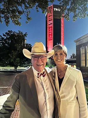 Chancellor Carine Feyten and husband Chad Wick stand outside the TWU ACT building lit up in maroon lights
