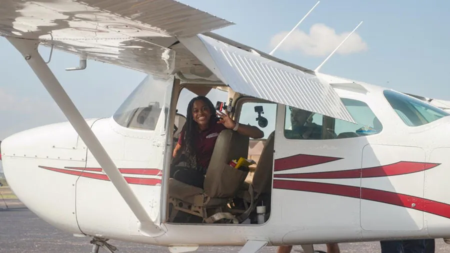 A member of the inaugural TWU aviation class sits inside of a small-engine plane on an airport tarmac
