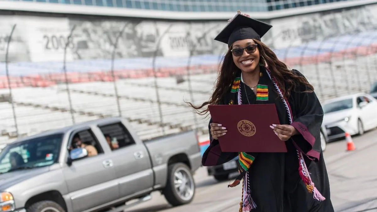 TWU graduate in cap and gown holding diploma at Texas Motor Speedway