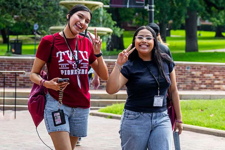 Two TWU students smile for a camera while walking on campus during Orientation.