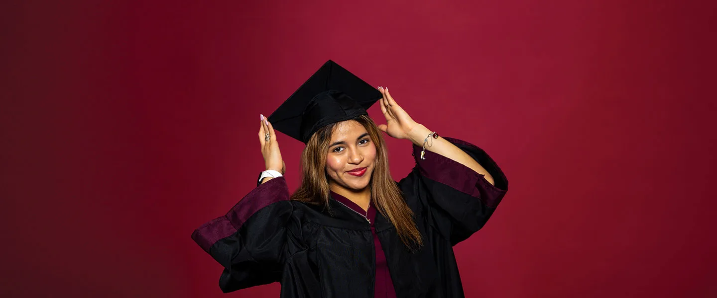 A portrait of a TWU student in graduation academic regalia on a maroon background.