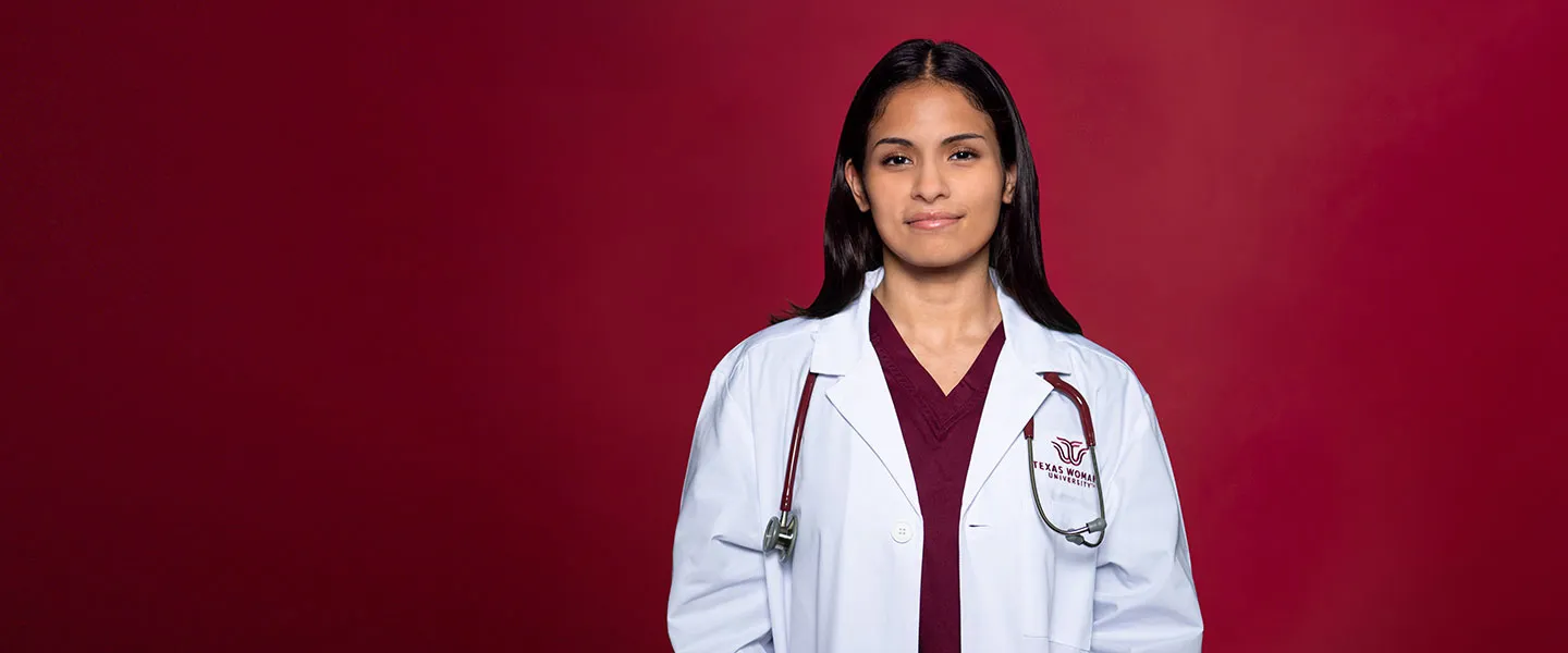 A TWU student wears maroon scrubs, a medical lab coat, and a stethoscope.