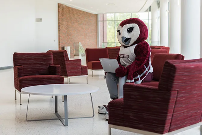 Oakley sits in a chair in the TWU Welcome Center and works on a laptop.